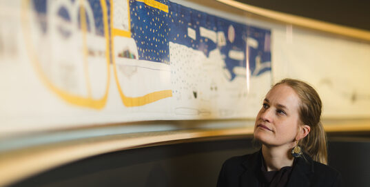 Ingeborg Høvik foran en kopi av Britta Marakatt-Labbas Historjá (originalen er på utlån). – Broderiet viser en sirkulær forståelse av tid og historie, der ånder, guder, gudinner og forfedre er med i nåtiden, sier hun.