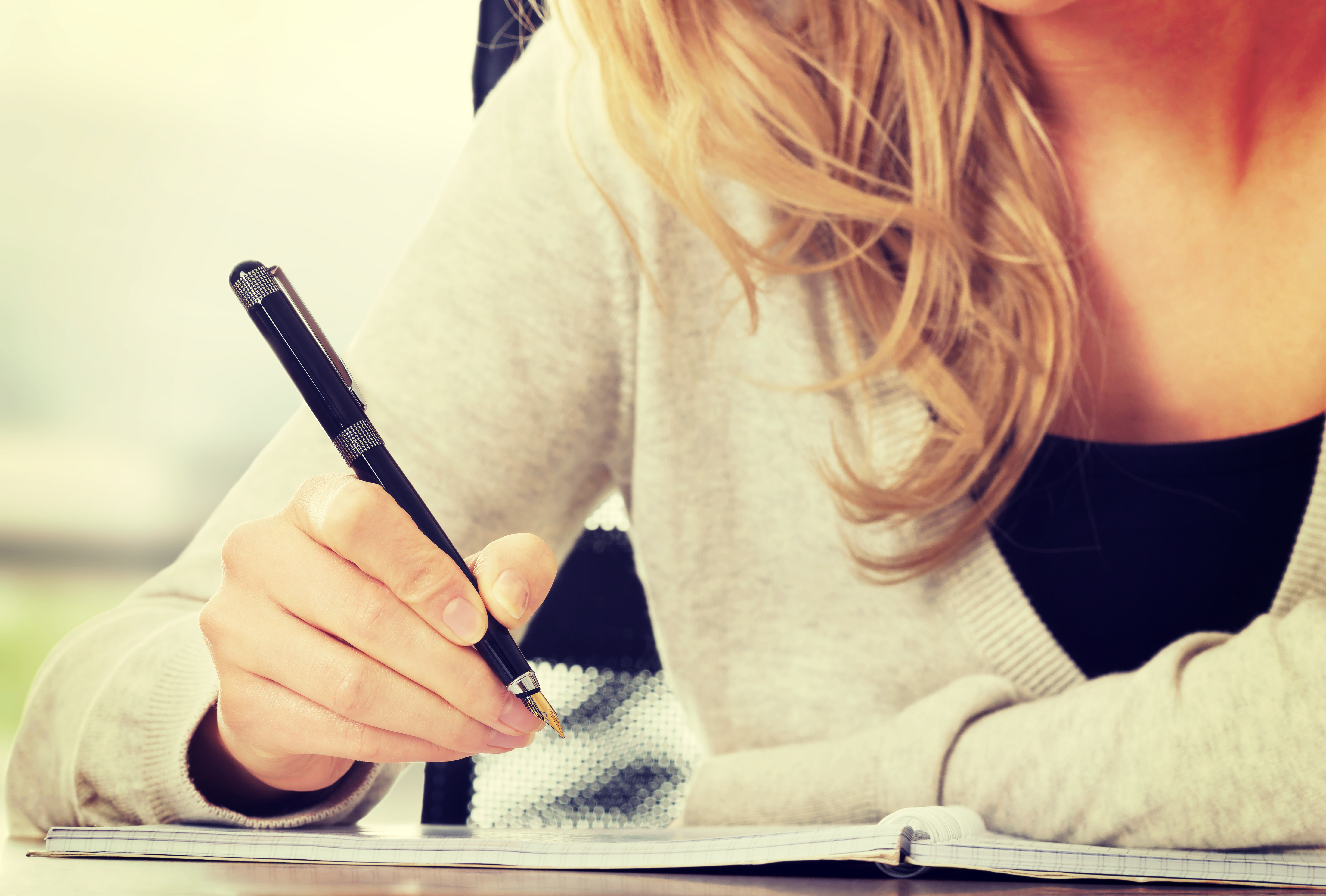 bildet viser en kvinne som skriver med penn i en bok