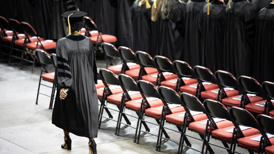 Rear view of a graduate student walking in black cap and gown at a college of law graduation ceremony.