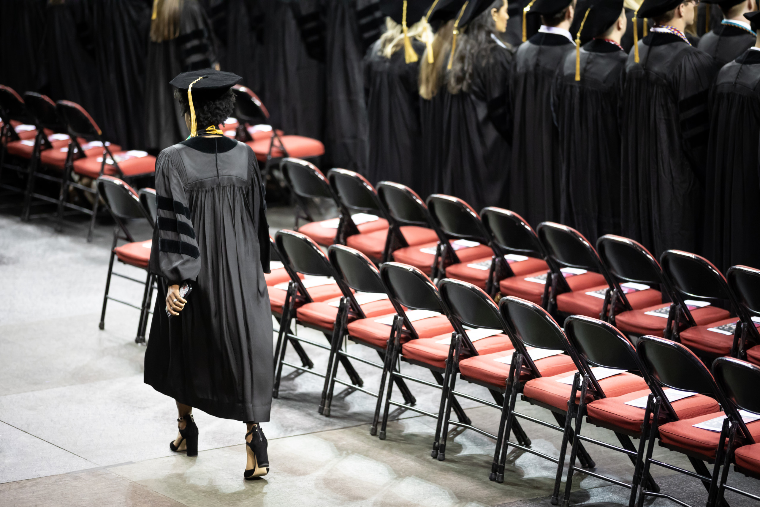 Rear view of a graduate student walking in black cap and gown at a college of law graduation ceremony.
