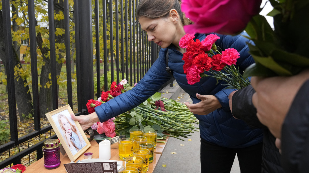 A woman puts a portrait of a victim of shooting next to flowers and candles outside the Perm State University following a campus shooting in Perm, about 1,100 kilometers (700 miles) east of Moscow, Russia, Tuesday, Sept. 21, 2021. A student opened fire at the university, leaving a number of people dead and injured, before being shot in a crossfire with police and detained. Beyond saying that he was a student, authorities offered no further information on his identity or a possible motive. (AP Photo/Dmitri Lovetsky)