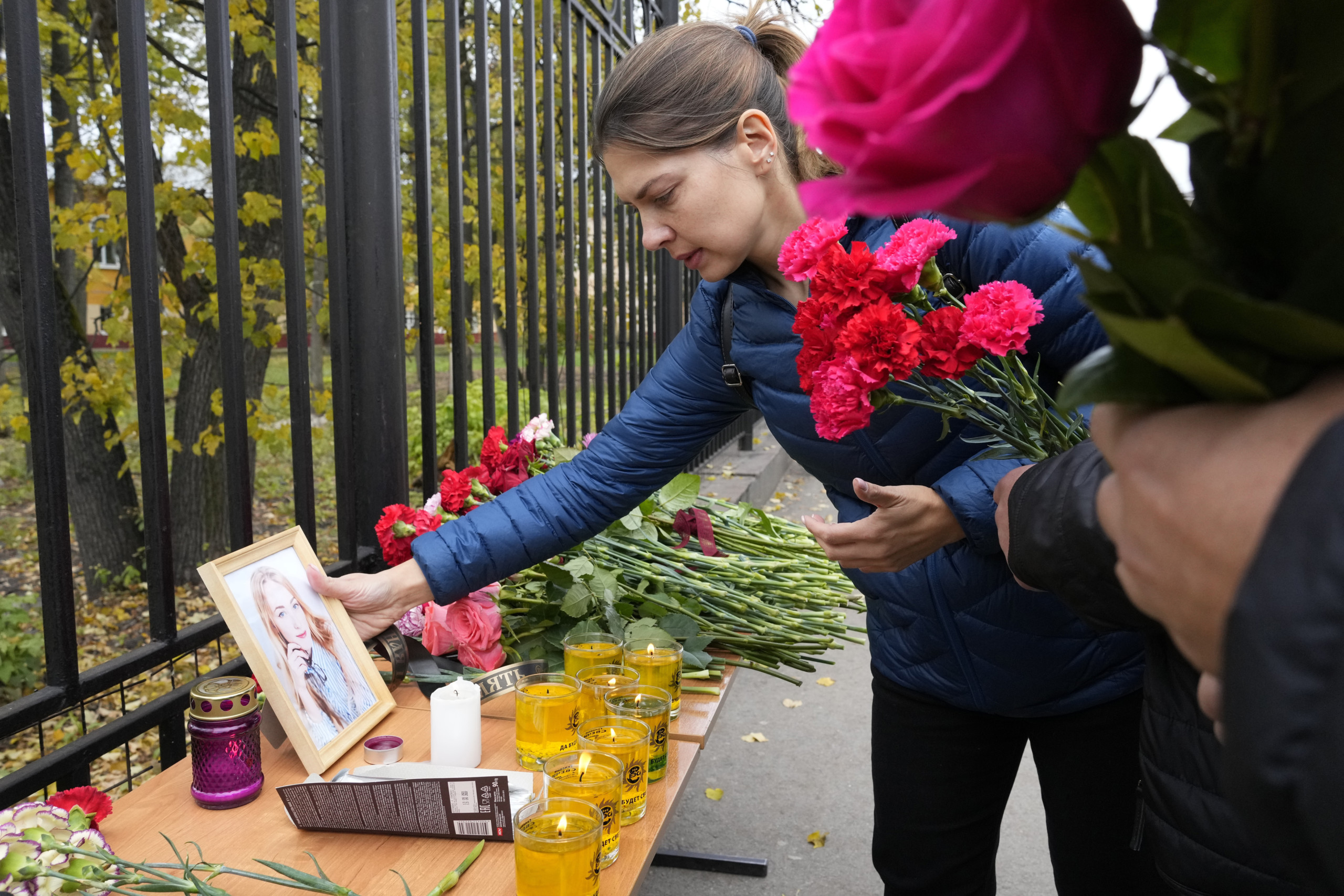 A woman puts a portrait of a victim of shooting next to flowers and candles outside the Perm State University following a campus shooting in Perm, about 1,100 kilometers (700 miles) east of Moscow, Russia, Tuesday, Sept. 21, 2021. A student opened fire at the university, leaving a number of people dead and injured, before being shot in a crossfire with police and detained. Beyond saying that he was a student, authorities offered no further information on his identity or a possible motive. (AP Photo/Dmitri Lovetsky)