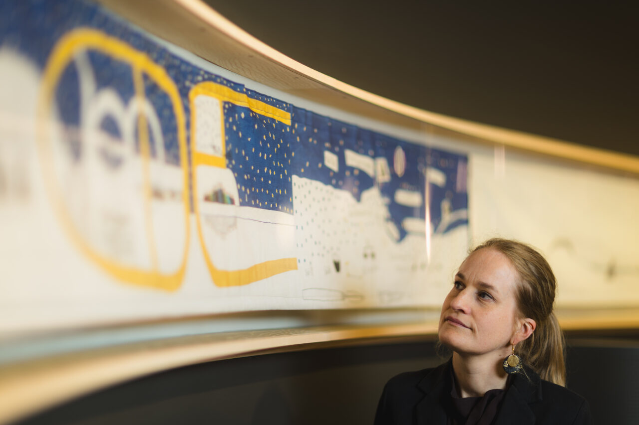 Ingeborg Høvik foran en kopi av Britta Marakatt-Labbas Historjá (originalen er på utlån). – Broderiet viser en sirkulær forståelse av tid og historie, der ånder, guder, gudinner og forfedre er med i nåtiden, sier hun.